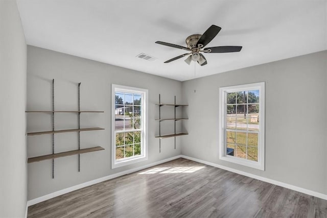 empty room with ceiling fan, plenty of natural light, and hardwood / wood-style floors