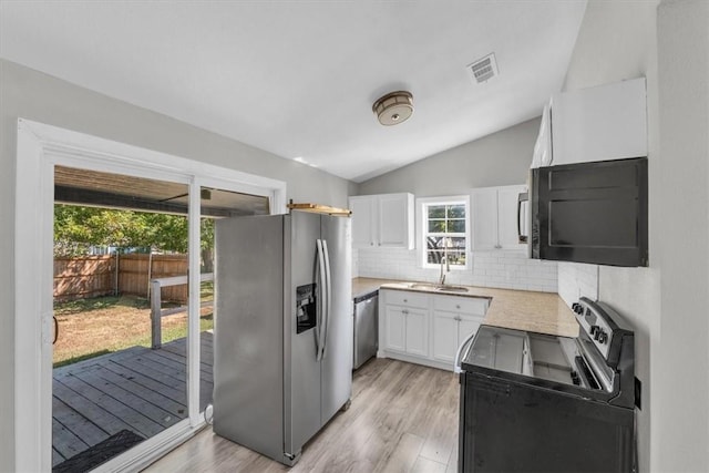 kitchen with white cabinetry, vaulted ceiling, decorative backsplash, appliances with stainless steel finishes, and light wood-type flooring