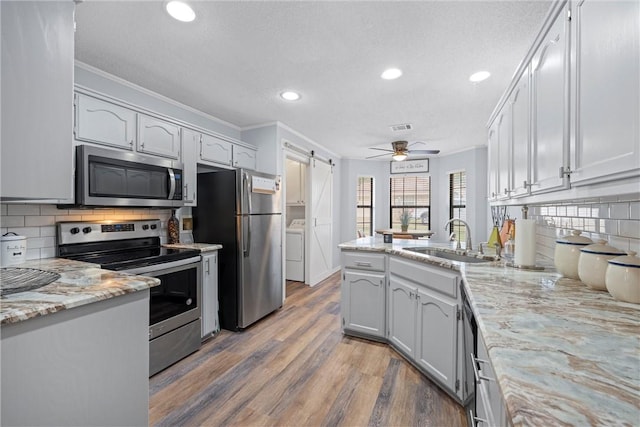 kitchen with sink, a barn door, kitchen peninsula, wood-type flooring, and appliances with stainless steel finishes