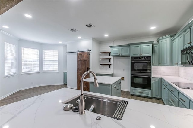 kitchen featuring a barn door, light stone countertops, sink, and black appliances