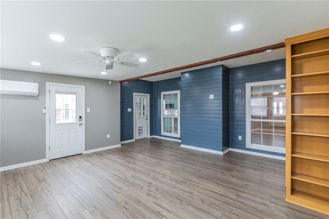 interior space with wood-type flooring, a wall mounted AC, ceiling fan, and wooden walls