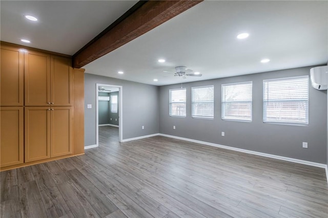 unfurnished living room with beamed ceiling, ceiling fan, a wall mounted AC, and light hardwood / wood-style flooring