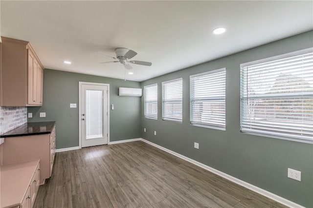 interior space featuring hardwood / wood-style flooring, ceiling fan, light brown cabinetry, and a wall unit AC