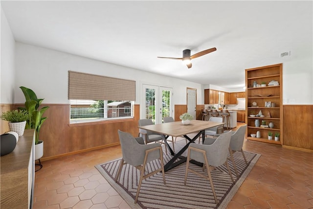 tiled dining room with wooden walls, french doors, and ceiling fan