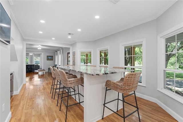 kitchen with plenty of natural light, light stone counters, light wood-type flooring, and a breakfast bar area