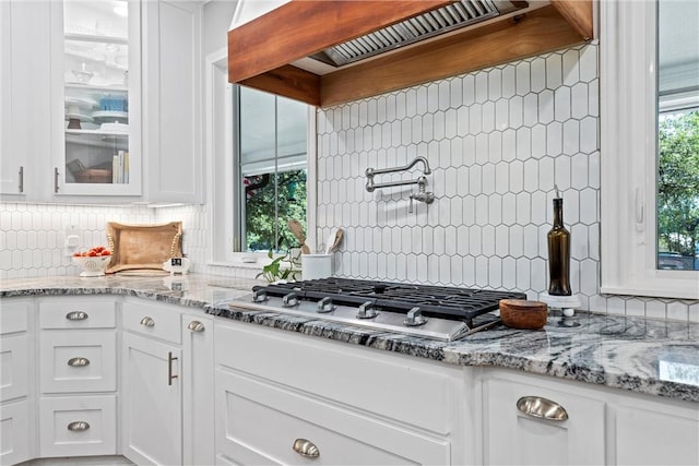 kitchen with stainless steel gas cooktop, light stone counters, backsplash, premium range hood, and white cabinets