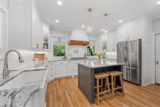 kitchen featuring custom range hood, stainless steel appliances, sink, white cabinets, and light hardwood / wood-style floors