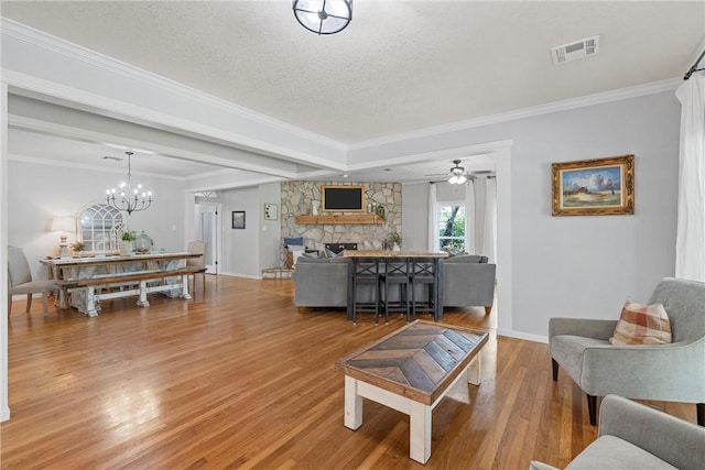 living room with ceiling fan with notable chandelier, hardwood / wood-style flooring, ornamental molding, a fireplace, and a textured ceiling