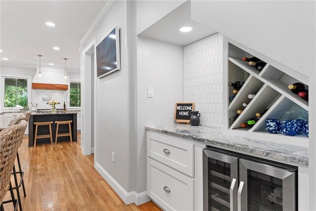 bar with light hardwood / wood-style flooring, light stone countertops, decorative light fixtures, white cabinetry, and beverage cooler