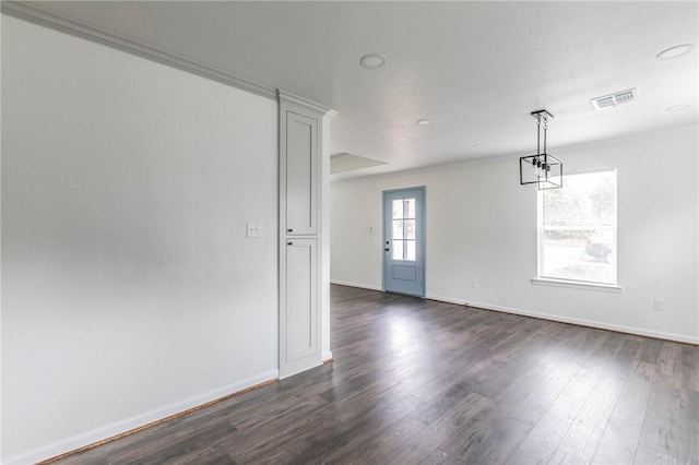 empty room with a textured ceiling, ornamental molding, and dark wood-type flooring