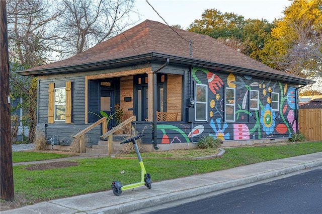 view of front of home with covered porch, roof with shingles, a front yard, and fence