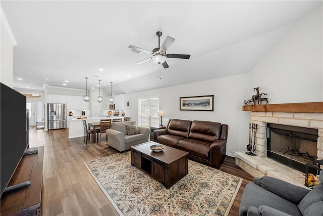 living room featuring a stone fireplace, ceiling fan, wood-type flooring, and vaulted ceiling