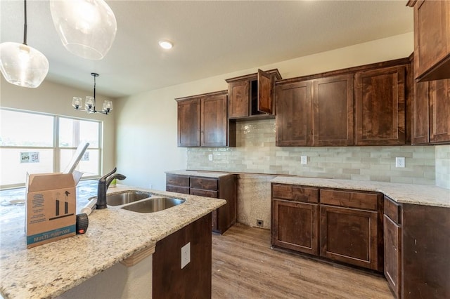 kitchen featuring sink, hanging light fixtures, light hardwood / wood-style flooring, tasteful backsplash, and a notable chandelier