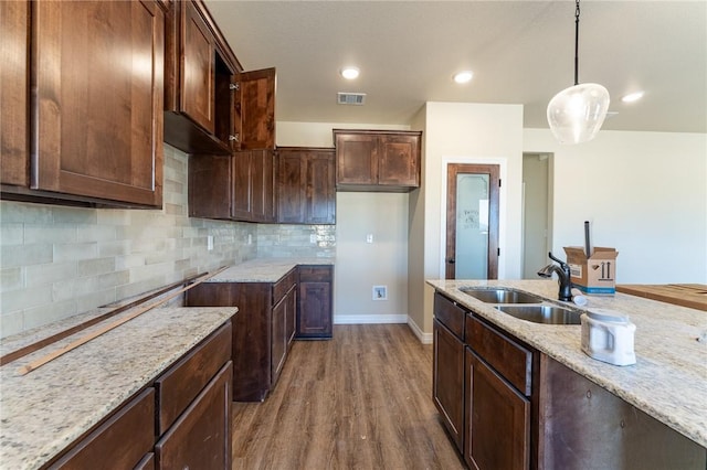 kitchen featuring backsplash, light stone counters, sink, pendant lighting, and hardwood / wood-style flooring