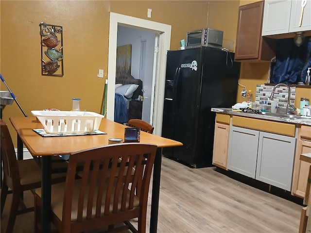 kitchen featuring white cabinetry, light countertops, a sink, and black fridge with ice dispenser