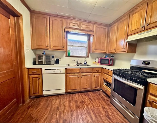 kitchen featuring dark wood-type flooring, under cabinet range hood, stainless steel range with gas stovetop, white dishwasher, and a sink