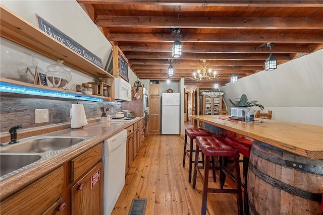 kitchen featuring white appliances, sink, hanging light fixtures, light wood-type flooring, and beam ceiling