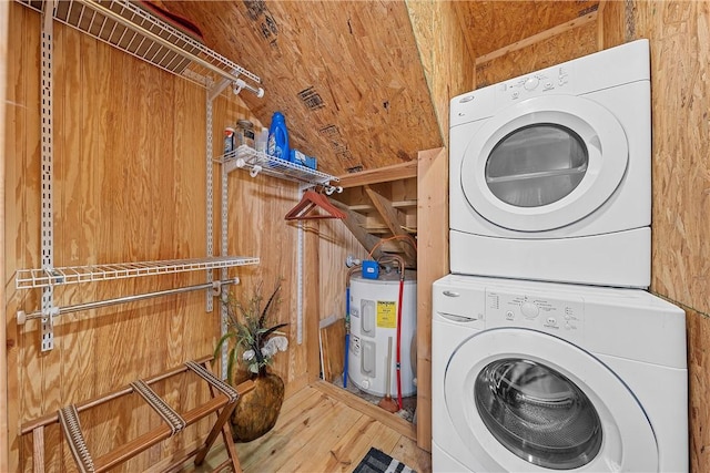 laundry area featuring water heater, wooden walls, wood-type flooring, and stacked washer / drying machine