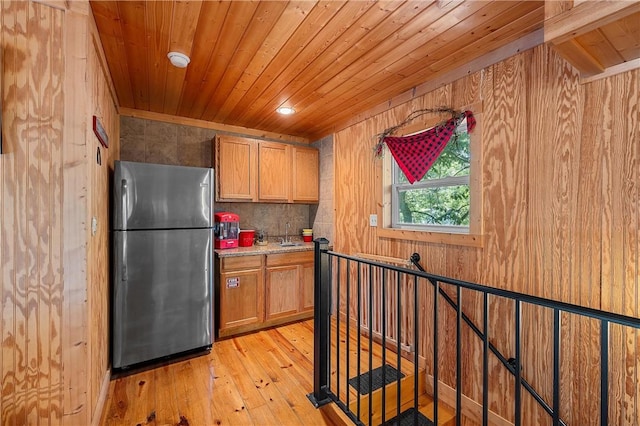 kitchen with wood walls, light wood-type flooring, stainless steel refrigerator, and wooden ceiling