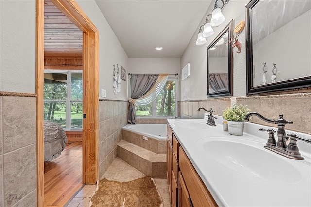 bathroom with tiled tub, vanity, tile walls, and hardwood / wood-style flooring