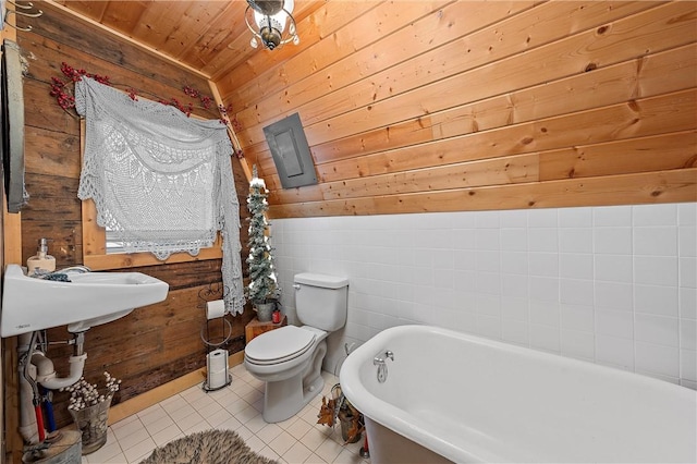 bathroom with a washtub, wooden ceiling, tile patterned floors, toilet, and wooden walls