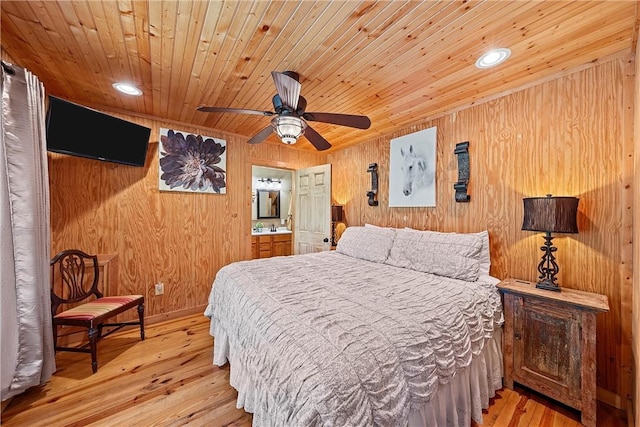 bedroom featuring connected bathroom, ceiling fan, light hardwood / wood-style flooring, and wood walls