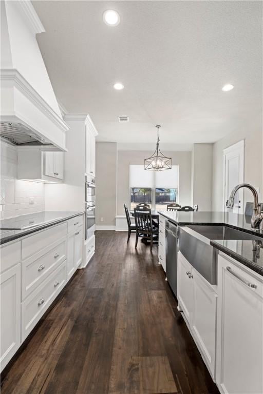 kitchen with dark hardwood / wood-style flooring, pendant lighting, white cabinets, custom exhaust hood, and appliances with stainless steel finishes