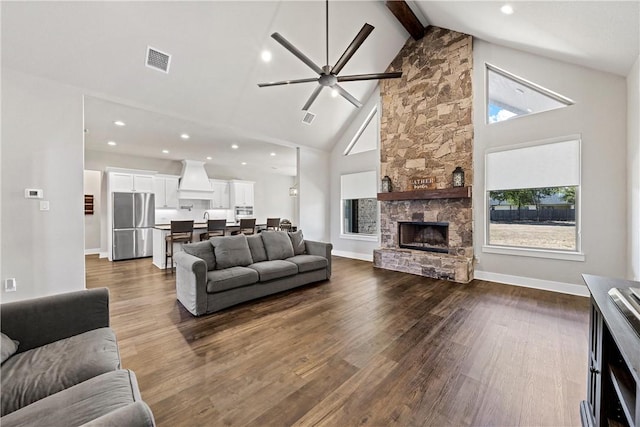 living room featuring ceiling fan, high vaulted ceiling, beamed ceiling, dark hardwood / wood-style floors, and a stone fireplace