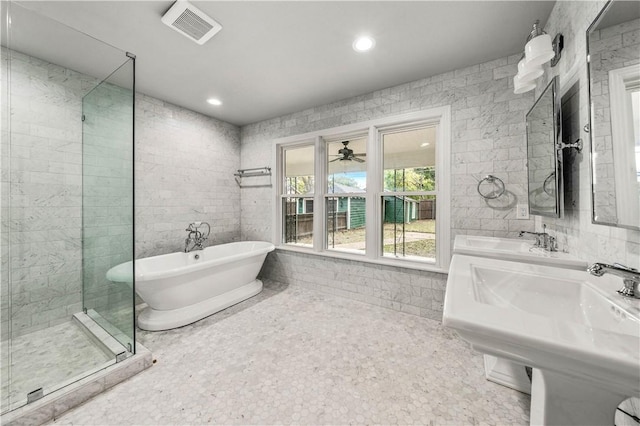 bathroom with dual sinks, tile walls, and plus walk in shower