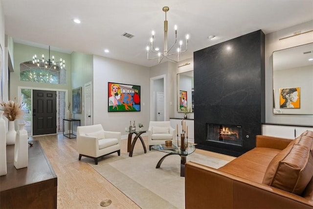 living room with a towering ceiling, light hardwood / wood-style flooring, a high end fireplace, and an inviting chandelier