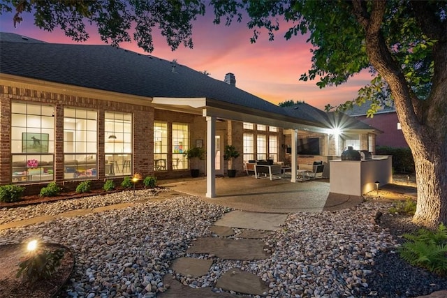 back house at dusk featuring an outdoor kitchen and a patio