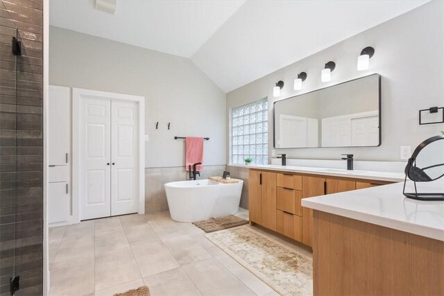 bathroom featuring tile patterned flooring, a tub to relax in, vaulted ceiling, vanity, and tile walls