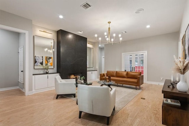 living room with a large fireplace, light hardwood / wood-style floors, and an inviting chandelier