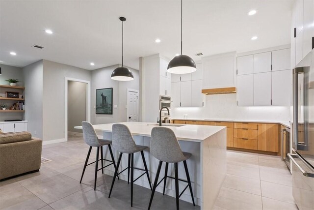 kitchen with a center island with sink, white cabinets, hanging light fixtures, and sink