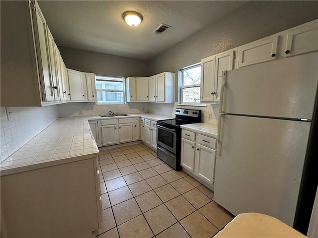 kitchen featuring visible vents, white cabinets, stainless steel range with electric cooktop, and freestanding refrigerator