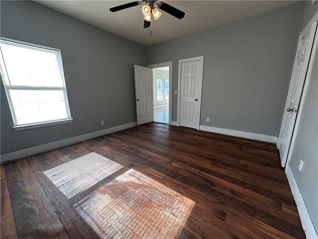 empty room with dark wood-type flooring, plenty of natural light, a ceiling fan, and baseboards