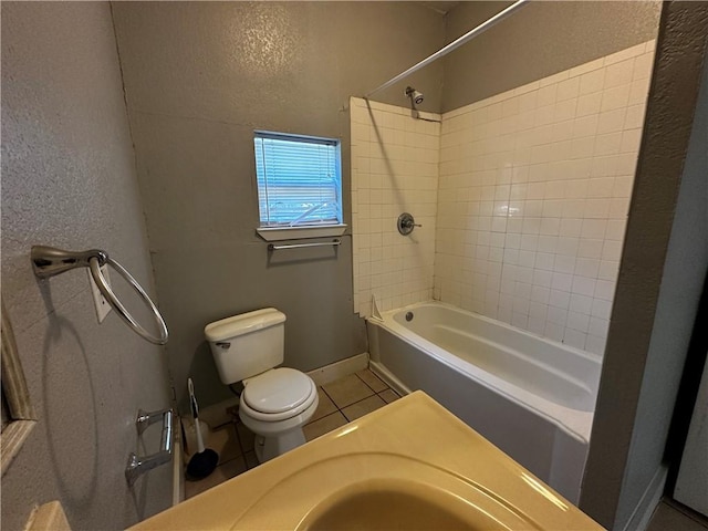 bathroom with shower / bath combination, baseboards, a textured wall, toilet, and tile patterned floors