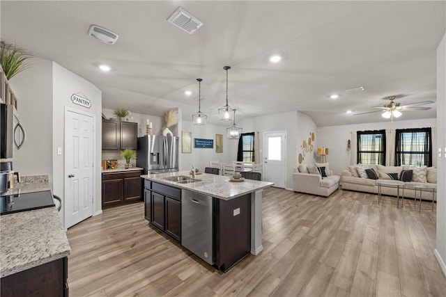 kitchen featuring decorative light fixtures, appliances with stainless steel finishes, open floor plan, dark brown cabinetry, and a sink