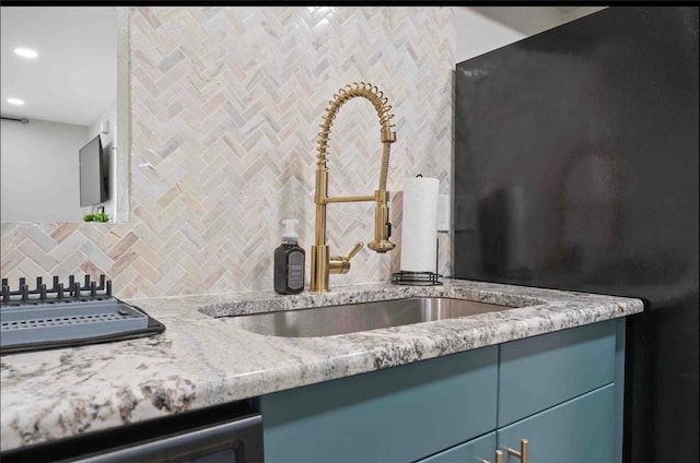 kitchen with blue cabinetry, dishwasher, light stone counters, decorative backsplash, and a sink