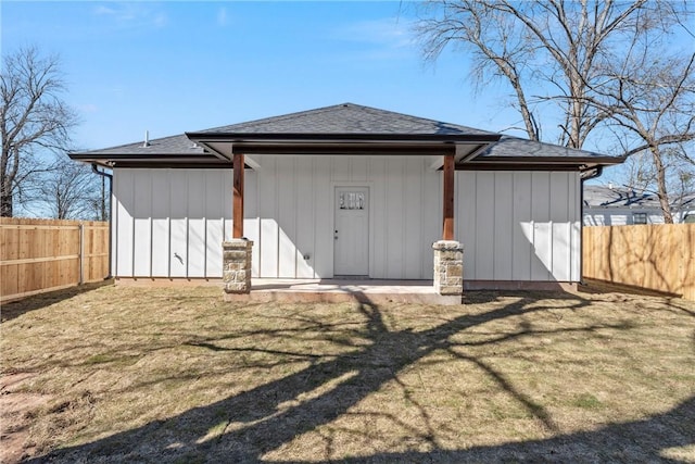 back of house featuring a yard, board and batten siding, fence, and roof with shingles