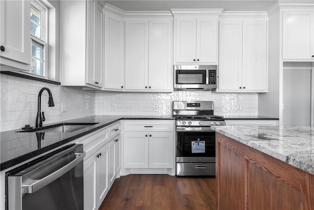 kitchen with light stone counters, appliances with stainless steel finishes, dark wood-type flooring, white cabinets, and a sink