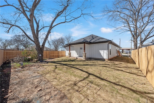 rear view of property featuring a shingled roof, a fenced backyard, and a lawn