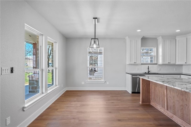 kitchen with wood finished floors, decorative backsplash, stainless steel dishwasher, light stone countertops, and baseboards