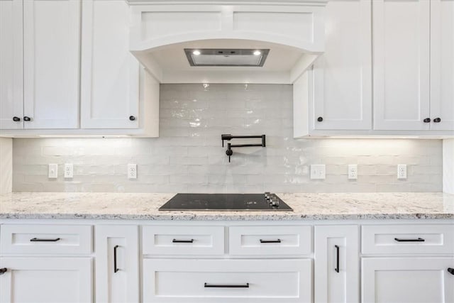 kitchen featuring white cabinets, custom range hood, black electric cooktop, and light stone counters