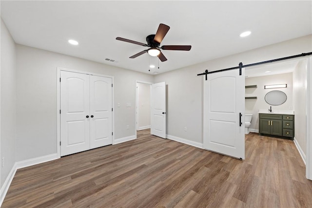 unfurnished bedroom featuring hardwood / wood-style flooring, a barn door, connected bathroom, and a closet