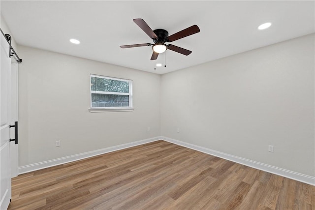 empty room with light wood-type flooring, a barn door, and ceiling fan