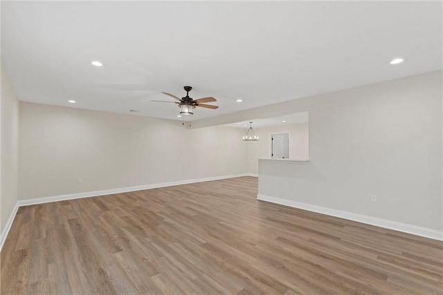 empty room featuring ceiling fan with notable chandelier and light wood-type flooring