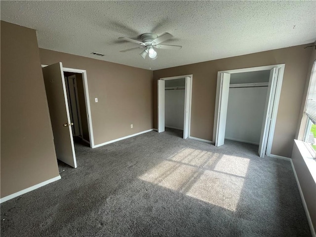 unfurnished bedroom with a textured ceiling, dark colored carpet, two closets, and ceiling fan