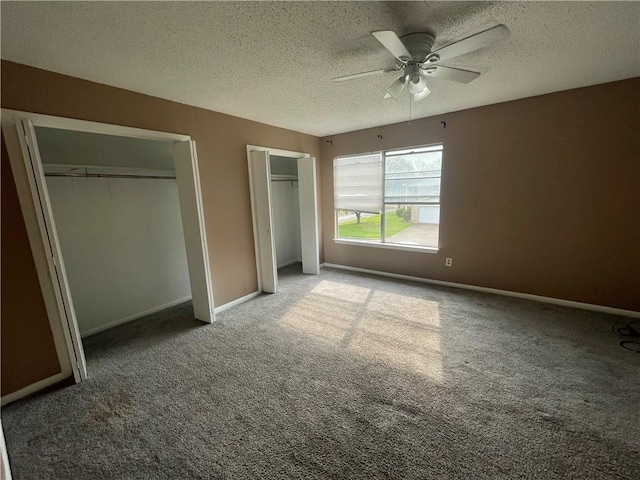 unfurnished bedroom featuring carpet floors, a textured ceiling, two closets, and ceiling fan