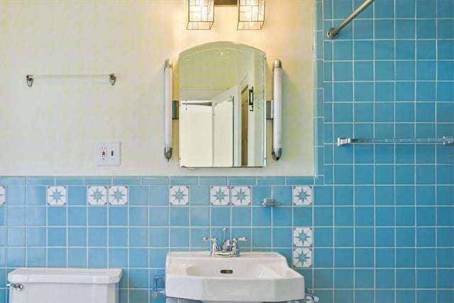 bathroom featuring a wainscoted wall, toilet, tile walls, and a sink